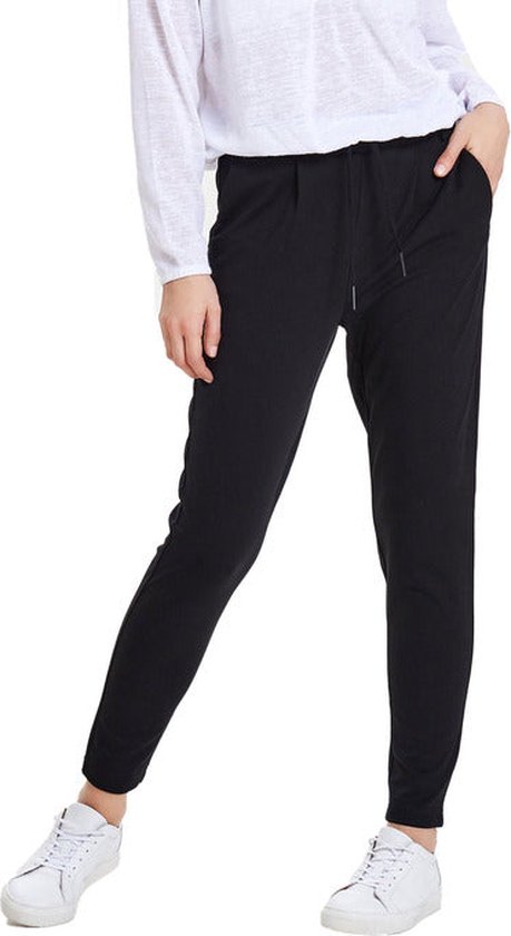 Zwarte, losvallende broek met ceintuur en witte sneakers, gedragen met een witte longsleeve.