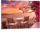 Dibond - Tafel met Stoeljes op Balkon met Roze Bloemenstruik met Uitzicht op Zee - 100x75 cm Foto op Aluminium (Wanddecoratie van metaal)