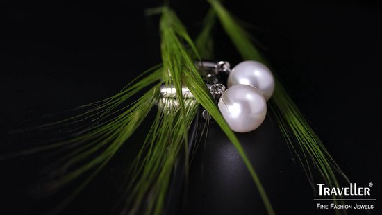 Twee zilverkleurige oorclips met parels liggen tussen groen gras. 'Traveller FINE FASHION JEWELS'.