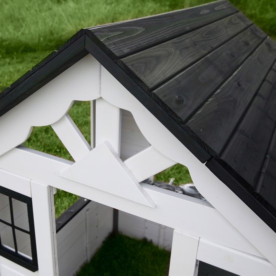 Detail van het zwarte houten dak van het witte speelhuis met decoratieve elementen.