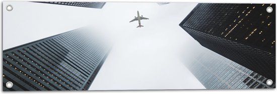 WallClassics - Tuinposter – Vliegtuig vliegend tussen Gebouwen - 90x30 cm Foto op Tuinposter (wanddecoratie voor buiten en binnen)