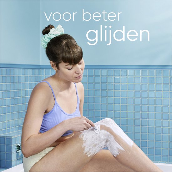 Vrouw scheert haar been in een badkamer met blauwe tegels. Ze heeft een blauw topje aan en scrunchies in haar haar. Tekst: 'voor beter glijden'.