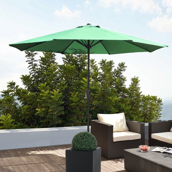 Groene parasol staat op een terras bij tuinmeubelen.