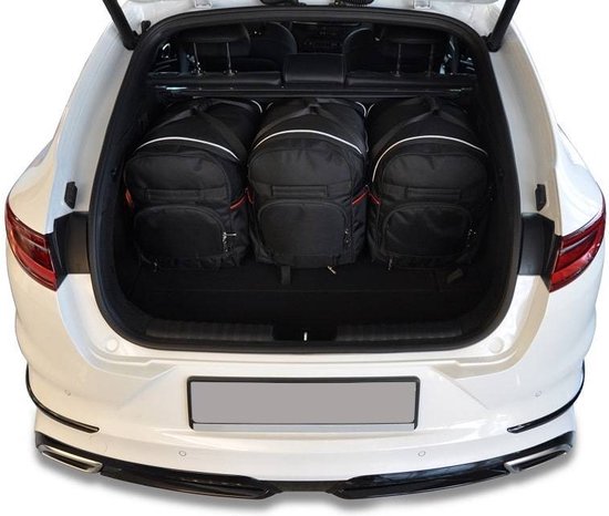Drie zwarte reistassen met witte en rode accenten in de kofferbak van een witte auto.
