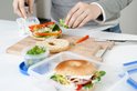 Une personne prépare un sandwich avec un bagel. Ingrédients et boîtes de conservation sur une planche à découper.