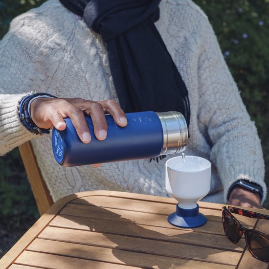 Persoon met sjaal schenkt drank uit Dopper Insulated fles in Breaker Blue in een wit bekertje.