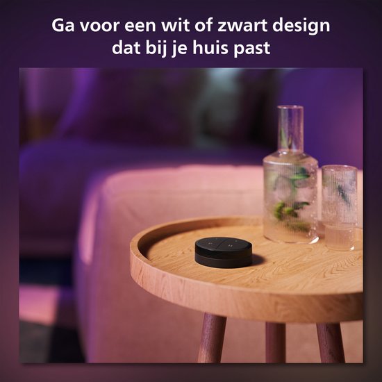 Zwarte Philips Hue Tap dial switch op een houten bijzettafeltje naast een glazen vaas.