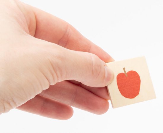 Een hand houdt een klein houten blokje vast met een rode appel erop.