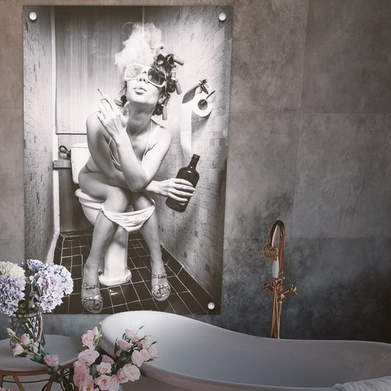 Zwart-wit foto van een vrouw op een toilet, rokend en met drank, naast een badkuip met bloemen.
