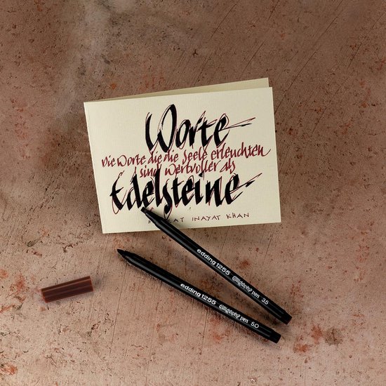 Zwarte Edding 1255 calligraphy pennen op een kartonnen kaart met sierlijke tekst.