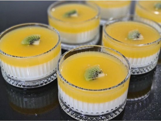 Vier glazen schaaltjes met witte pudding en gele topping, gegarneerd met plakjes kiwi.