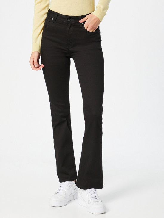 Vrouw in zwarte flared jeans met een lichtgele coltrui en witte sneakers.