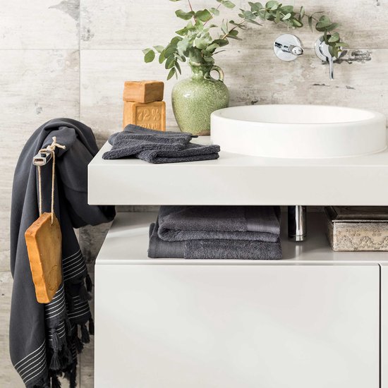Serviettes gris foncé sur un lavabo blanc avec un vase vert et du savon.