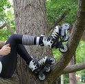 Een persoon zit in een boom, met op rolschaatsen met witte schoenen, gouden en zwarte details en drie wielen.