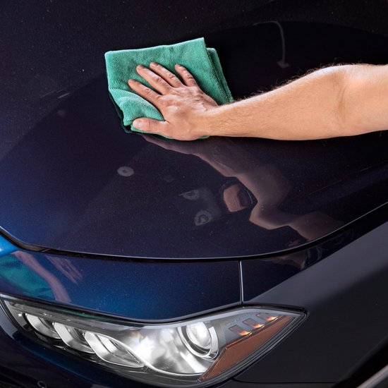 Main avec un chiffon microfibre vert nettoyant le capot d'une voiture bleu foncé.