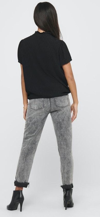 Model van achteren in een zwarte blouse met korte mouwen, ruchekraag en strikdetail, met een grijze jeans en zwarte laarsjes.