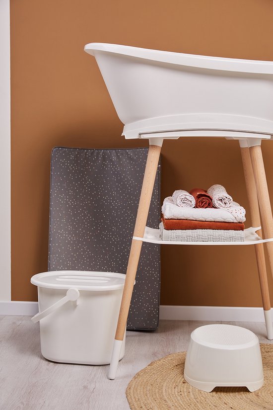 Witte babymediatoren met houten poten. Onder de badkuip liggen witte handdoeken en bruine en oranje babykleding. Naast de badkuip staat een grijze luieremmer met stippen.