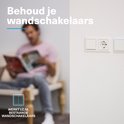 Een man leest een tijdschrift, op de voorgrond een detail van een witte Nederlandse schakelaar en stopcontact.