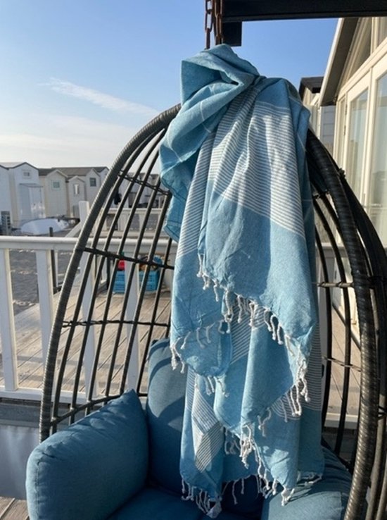 Turquoise hamamdoek met witte strepen en franjes, hangend over een schommelstoel buiten.