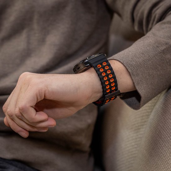 Zwart en oranje siliconen horlogebandje met ronde perforaties om de pols.