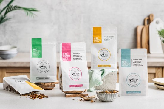 Vier zakken XAVIES' Granola op houten en stenen ondergronden. De zakken zijn wit met gekleurde labels: groen, roze, geel en cyaan.