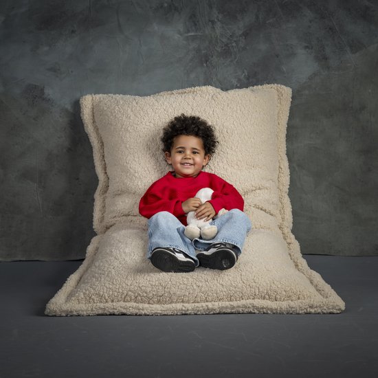 Jongetje zit op een groot, crèmekleurig teddy zitkussen.