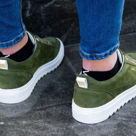 Benen in spijkerbroek en groene sneakers, met zwarte lage sokken.