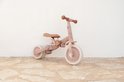 Roze loopfiets met bloemenprint, staand tegen een witte muur.