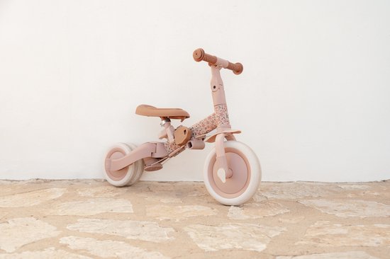 Roze loopfiets met bloemenprint, staand tegen een witte muur.