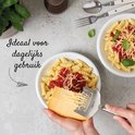 Des mains râpent un bloc de fromage avec une râpe à fromage argentée sur une assiette de pâtes avec sauce et fromage.