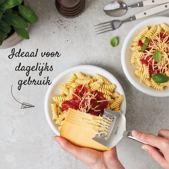 Des mains râpent un bloc de fromage avec une râpe à fromage argentée sur une assiette de pâtes avec sauce et fromage.