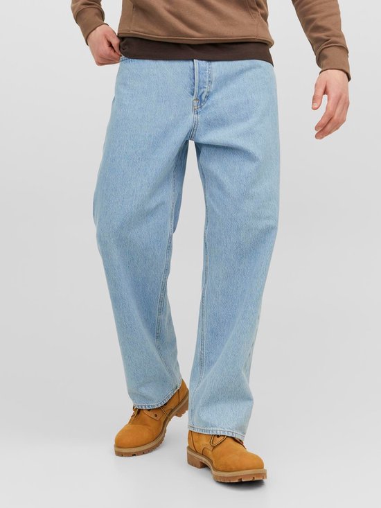 Man in een lichtblauwe loose-fit jeans met bruine laarzen en een bruine hoodie.