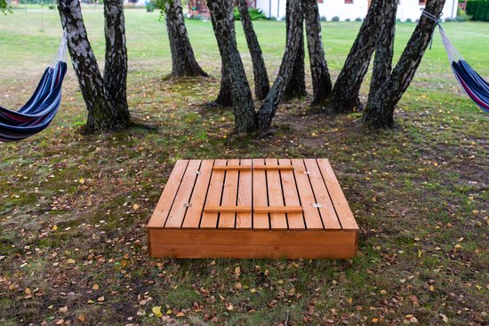 Houten zandbak met gesloten houten deksel in een tuin met bomen.