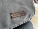 Close-up van een bruin label met "Jaxx World" op grijze stof.