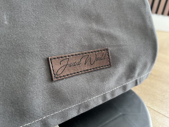 Close-up van een bruin label met "Jaxx World" op grijze stof.