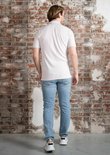 Een man staat met zijn rug naar de camera, hij draagt een lichtpaars poloshirt en een lichte jeans.