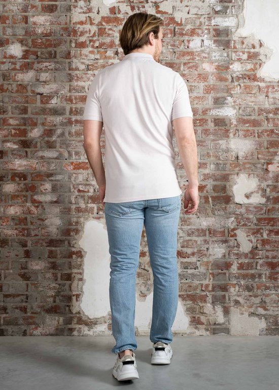Een man staat met zijn rug naar de camera, hij draagt een lichtpaars poloshirt en een lichte jeans.