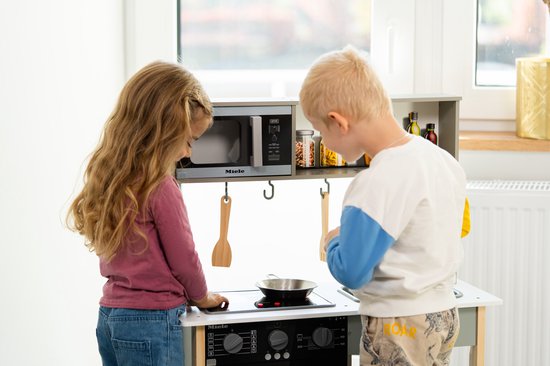 Jongen en meisje spelen met een witte houten speelkeuken, met de achterkant naar de camera.