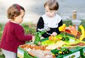 Twee kinderen spelen met een John Deere boerderij speeltafel met groen/gele tractoren en boerderijdieren.