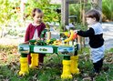 Een jongen en meisje spelen bij een John Deere boerderij speeltafel met diverse speelgoedvoertuigen.