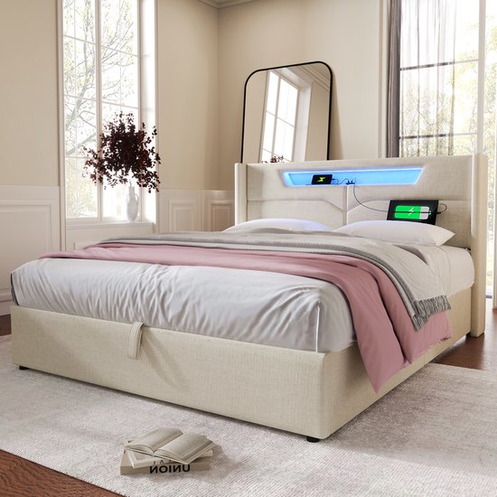 Lit rembourré beige avec espace de rangement, éclairage LED et ports USB dans la tête de lit. Un plaid rose est drapé sur le lit.