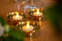 Drie LED waxinelichtjes in gouden houders op een houten tafel.