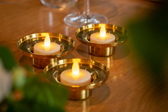 Drie LED waxinelichtjes in gouden houders op een houten tafel.