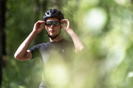 Man met zwarte fietshelm en sportbril met gespiegelde glazen past de bril aan.