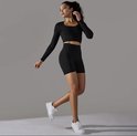 Model in een zwarte longsleeve crop top en zwarte biker shorts, gedragen met witte sneakers.