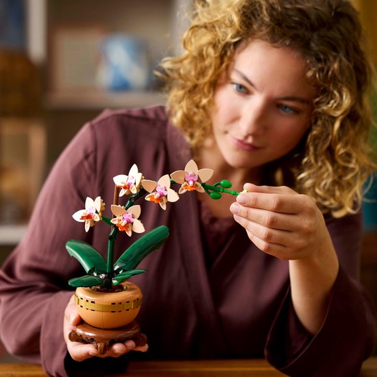 Een vrouw met krullend haar houdt een LEGO-orchidee vast, met tekst 'Vol authentieke details voor een levensechte look'.