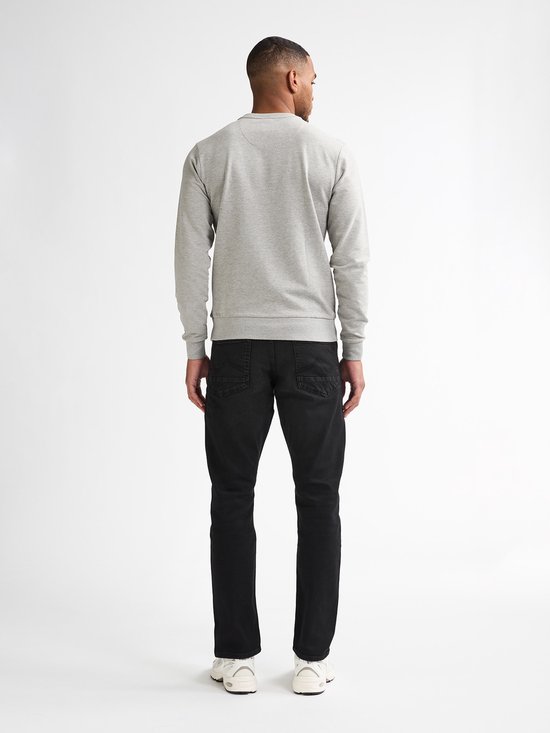 Man van achteren gezien, draagt een grijze sweater en zwarte jeans.