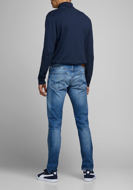 Man van achteren gezien, draagt een donkerblauwe coltrui en een spijkerbroek.