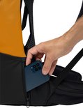 Hand doet smartphone in een ritsvak van een oranje rugzak met gaasdetails.