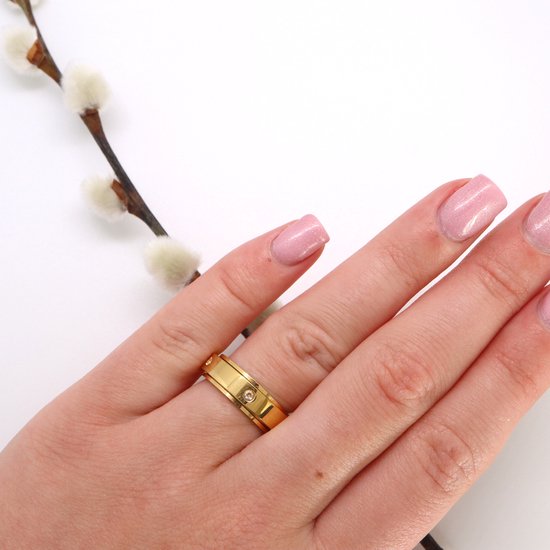 Gouden ring met vier kleine steentjes, gedragen om een hand met roze nagels.